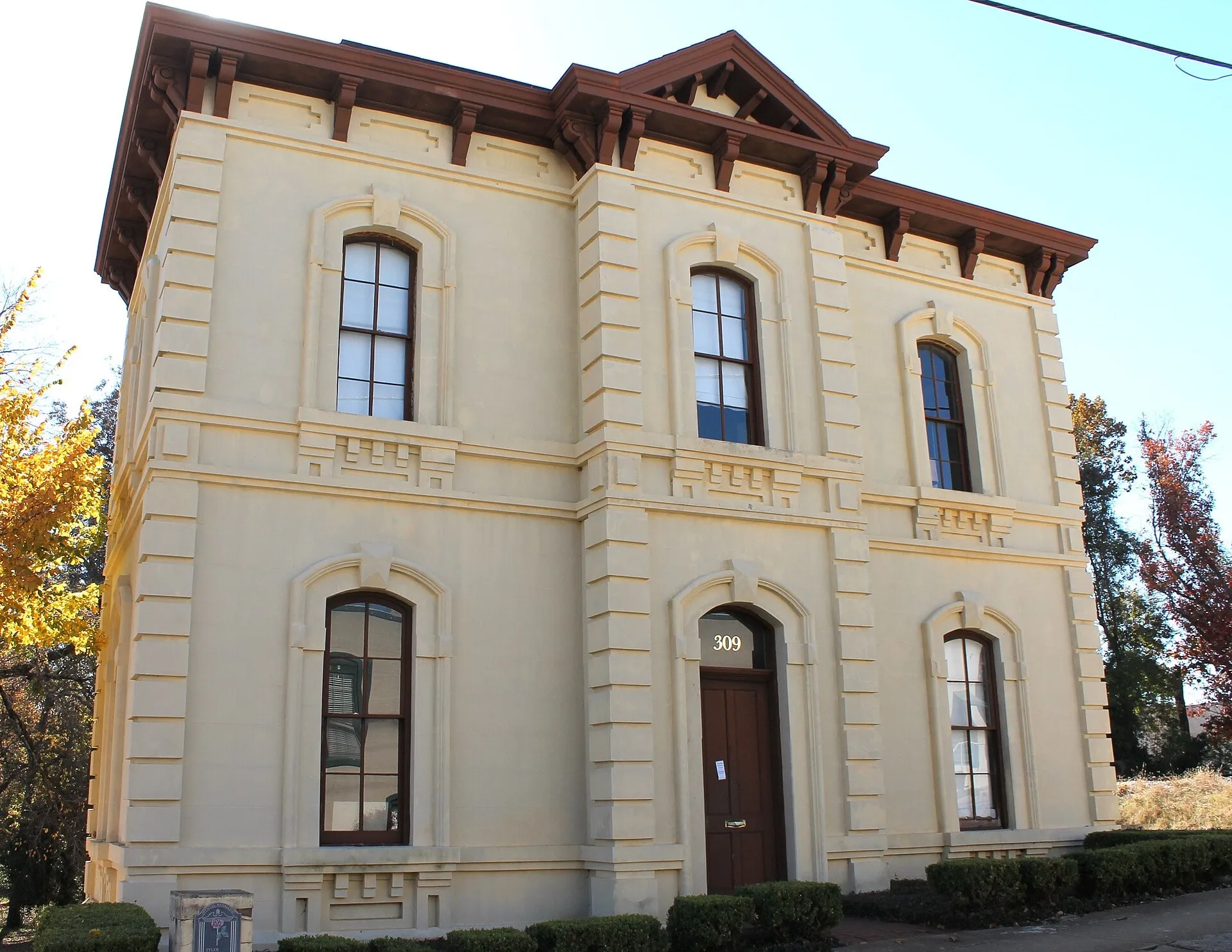 A two-story cream-colored building with tall arched windows, quoined corners and a bracketed cornice.