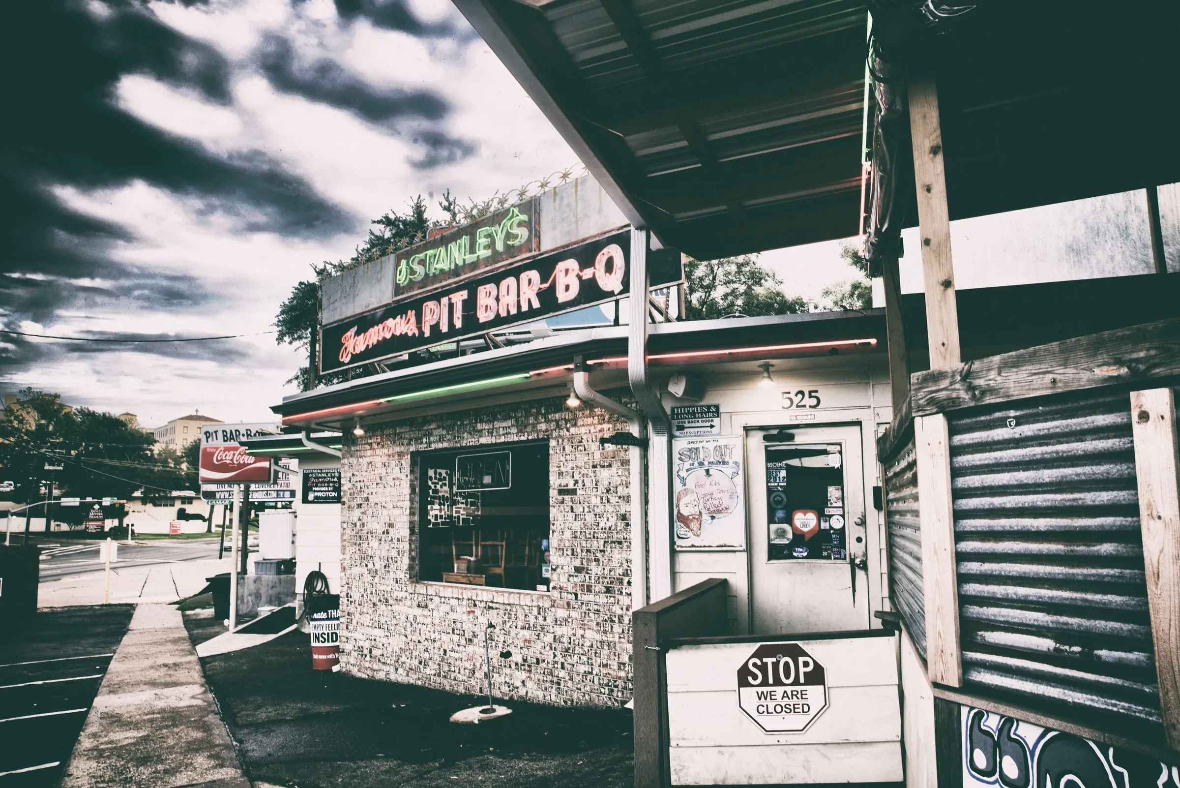 A small brick barbecue stand under a neon sign that reads Stanley’s Famous Pit Bar-B-Q, in a high-contrast photograph.